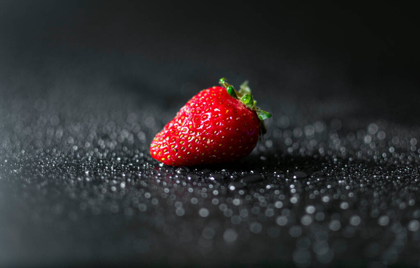 Un seul fraisier rouge frais et juteux sur fond noir avec des gouttes d'eau. - Photo, image
