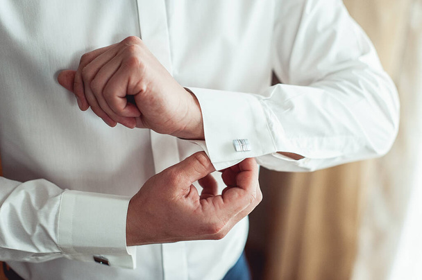 A man fastens cufflink on the white shirt. Close up of a man hand wearing a white shirt and cufflinks. - Fotó, kép