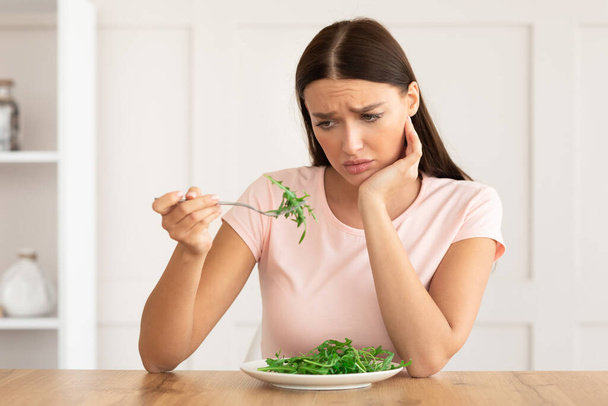 Δυστυχισμένη γυναίκα κουρασμένος από τη διατροφή τρώει πράσινη σαλάτα στο σπίτι - Φωτογραφία, εικόνα