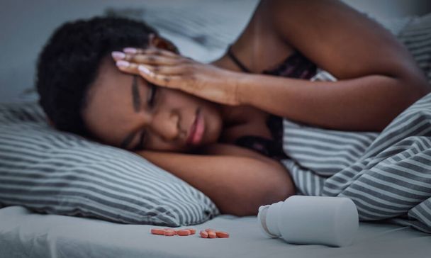 Pillereitä sirotellaan purkista sängyllä, afrikkalainen amerikkalainen tyttö ei voi nukahtaa
 - Valokuva, kuva