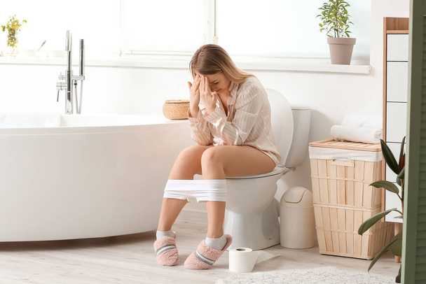 Jeune femme avec des hémorroïdes assis sur un bol de toilette à la maison
 - Photo, image