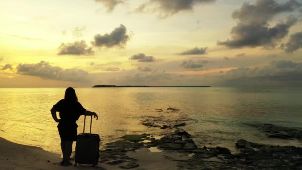 Silhouet van een vrouw tegen een zonsondergang met bagage op het strand - Video