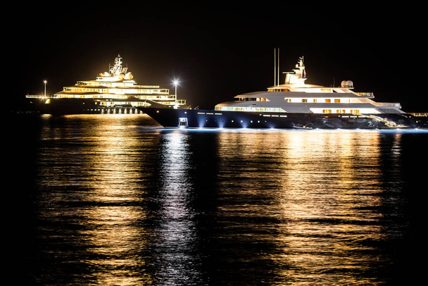 Δύο βάρκες στέκονται στο νερό τη νύχτα. Το φως των φώτων τους αντανακλά στο νερό.. - Φωτογραφία, εικόνα