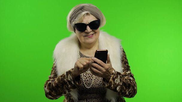 Ouderen stijlvol trendy Kaukasische oma vrouw met behulp van smartphone. Chromatoetsen - Foto, afbeelding