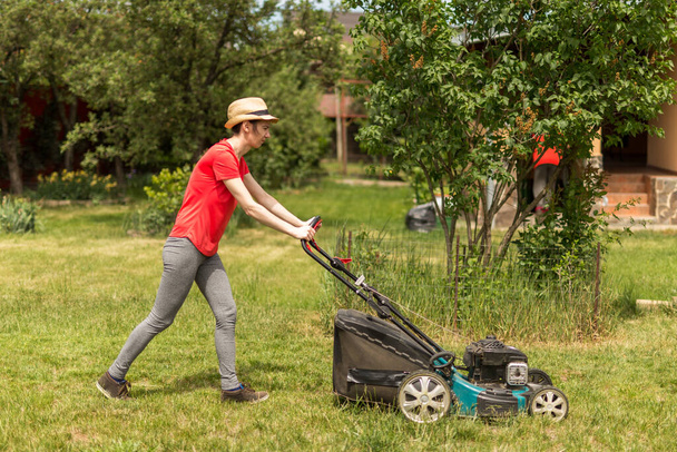 Güneşli bir günde arka bahçesinde çim biçme makinesiyle çim biçen bir kadın.. - Fotoğraf, Görsel