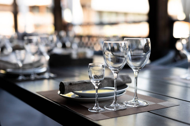 Mesa festiva con copas vacías. Banquete de selebración con servilletas, platos y anteojos marrones para vino blanco y tinto en la mesa de madera
 - Foto, Imagen