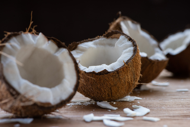 селективный фокус свежих вкусных кокосовых половинки и хлопья на деревянном столе изолированы на черном
 - Фото, изображение