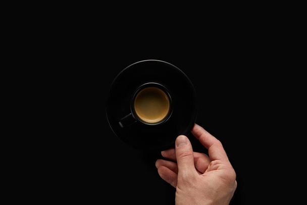 Jongeman 's hand serveert een zwarte kop koffie op een zwarte tafel - Foto, afbeelding