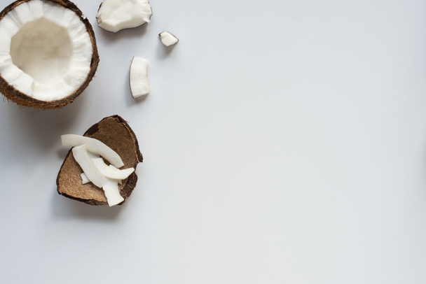 vrchní pohled na čerstvé chutné popraskané kokosové poloviny s vločkami a skořápkou na bílém pozadí - Fotografie, Obrázek
