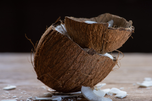 selective focus of fresh tasty coconut half and flakes in shell on wooden table isolated on black - Foto, immagini