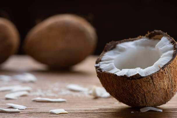 selective focus of fresh tasty coconut half and flakes on wooden table isolated on black - Foto, Bild