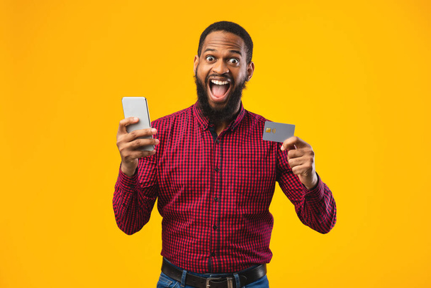 Черный мужчина держит кредитку и мобильный телефон в студии
 - Фото, изображение