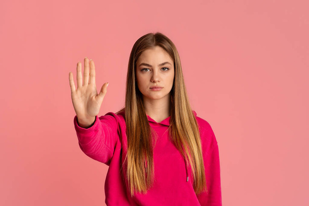 Basta de gestos. Estricta adolescente en sudadera con capucha rosa levanta la mano
 - Foto, imagen