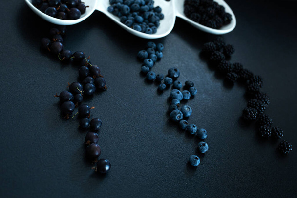 Set of different types of black berries in a white plate on a black table. Stylish seasonal vitamins. - Foto, Imagen