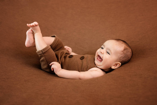 Söpö vastasyntynyt vauva ruskealla peitolla. Hymyilevä vauva tummalla taustalla. Lähikuva muotokuva vastasyntyneen vauvan. Vauvan tavaroiden pakkausmalli. Lastenhuone. Lääketieteellinen ja terve käsite
. - Valokuva, kuva
