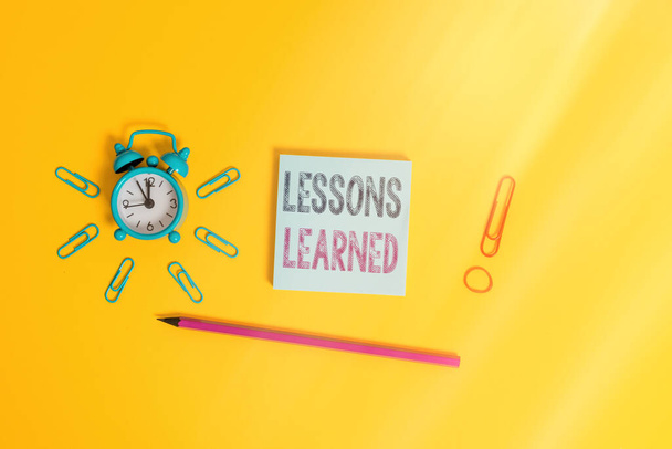 Writing note showing Lessons Learned. Business photo showcasing the knowledge or understanding gained by experience Alarm clock wakeup clips rubber band pencil notepad colored background. - Photo, Image
