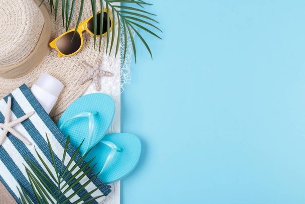 青い背景、サングラス、日焼け止め、フリップフロップ、タオルと帽子、夏休みのコンセプト、コピースペースのビーチアクセサリー - 写真・画像