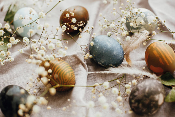 Stilvolle Ostereier auf rustikalem Tisch. Natürlich gefärbte bunte Ostereier mit frühlingshaften weißen Blüten und Federn auf ländlichem Textilhintergrund. Raum für Text - Foto, Bild