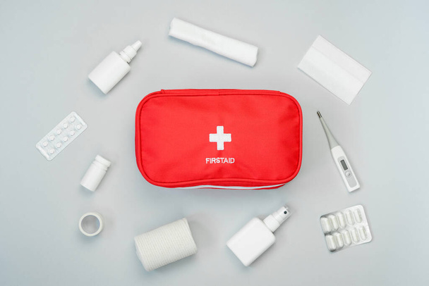 First aid kit red bag with medical equipment and medications for emergency treatment. Top view flat lay on gray background. - Foto, immagini