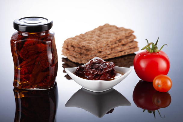 Dried tomatoes in olive oil preserved in a glass jar on a light background. - Photo, Image