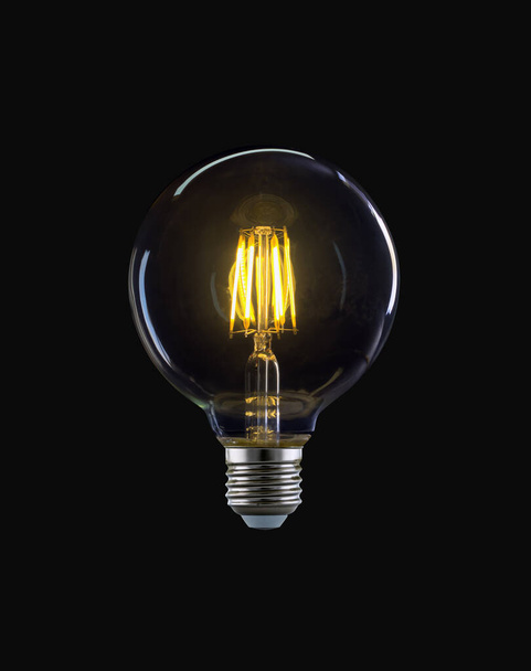 Bulb with transparent round balloon and yellow light isolated on black background. - Photo, Image