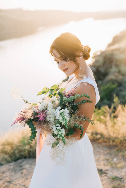 Novia en un lujoso vestido de novia blanco en la naturaleza al atardecer
 - Foto, Imagen