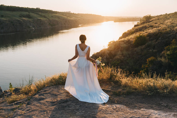 日没時に自然の中で豪華な白いウェディングドレスで花嫁 - 写真・画像