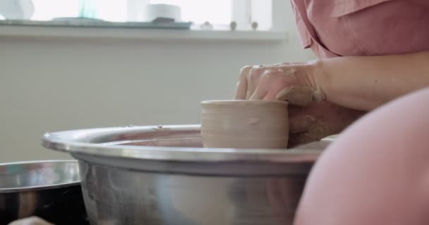 Vrouwelijke pottenbakker zit en maakt een kopje op het aardewerk wiel. Een vrouw die keramiek maakt. Pottenbakken, handgemaakte en creatieve vaardigheden - Video