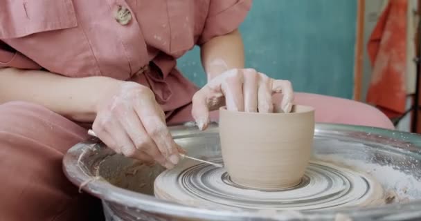 Female potter sitting and makes a cup on the pottery wheel. Woman making ceramic item. Pottery working, handmade and creative skills - Footage, Video