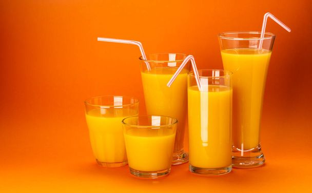 オレンジジュースのグラスは、テキスト、新鮮な柑橘類のカクテルのためのコピースペースとカラーオレンジの背景に隔離された - 写真・画像