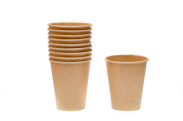 Una taza de papel marrón para café, té, una bebida hecha de materiales ambientales. Una pila de vasos pegados en uno en un soporte junto a una taza sobre fondo blanco, negro y amarillo
 - Foto, imagen