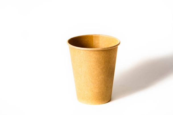 Taza de papel marrón para café, té, una bebida de materiales ambientales sobre un fondo blanco. Una taza de papel está a la derecha y una sombra cae sobre ella sobre un fondo blanco
. - Foto, imagen