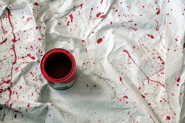 Uma folha de poeira decoradores com salpicos de tinta vermelha vibrante em torno de uma lata de tinta aberta
. - Foto, Imagem