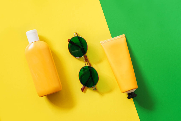 Summer bright flatlay on colorful background with tubes and bottle with sunscreen, green sunglasses. Hard shadows and light. Top view. Flat lay. Trend style. Copyspace. - Valokuva, kuva