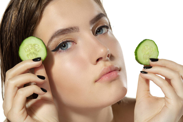 Close-up van mooie jonge vrouw met komkommer plakjes over witte achtergrond. Cosmetica en make-up, natuurlijke en eco-behandeling, huidverzorging. - Foto, afbeelding