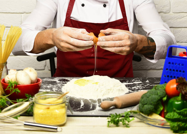 Male hands break egg into flour on white brick background - Photo, Image