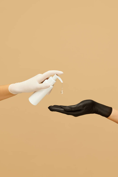Personal Hygiene. Female Hand In White Glove Holding Gel Sanitizer Bottle On Beige Background. Washing Hands For Virus Prevention And Staying Healthy.  - Photo, Image