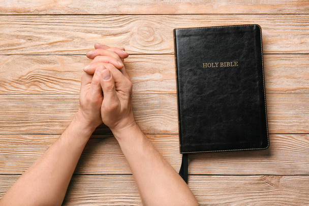 İncil 'i olan bir adamın elleri masada dua ediyor. - Fotoğraf, Görsel