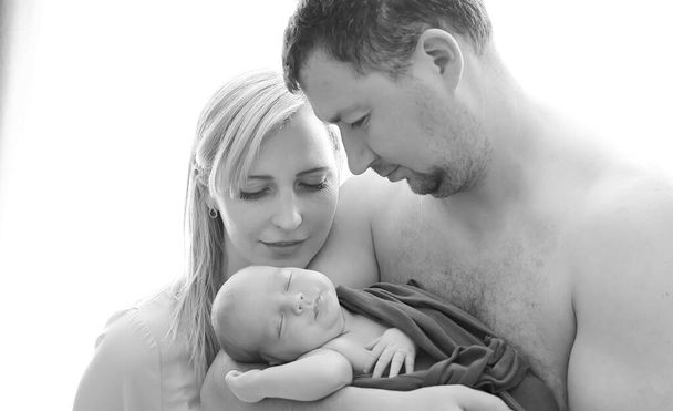 Γυναίκα και άντρας κρατούν ένα νεογέννητο. Μαμά, μπαμπά και μωρό. Πορτρέτο μιας χαμογελαστής οικογένειας με ένα νεογέννητο στην αγκαλιά της. Η έννοια της ευτυχισμένης οικογένειας.  - Φωτογραφία, εικόνα