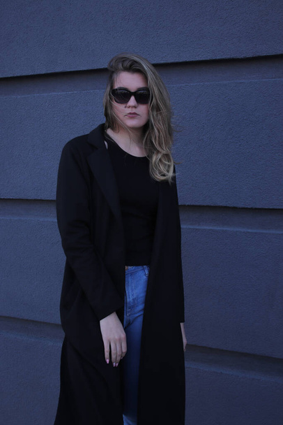 городской портрет задумчивой флиртующей красивой женщины в черной блузке и джинсах на фоне серой стены в полосках
 - Фото, изображение
