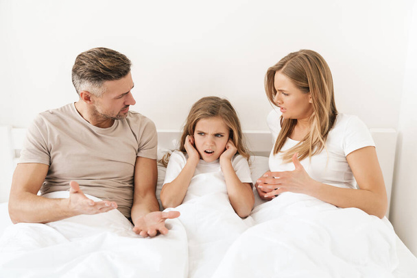 Photo of displeased caucasian parents scolding their stressed daughter while sitting in white bad - Fotoğraf, Görsel