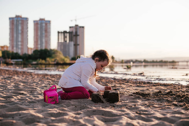 a girl plays with sand on a sandy beach on the river Bank during sunset - Fotoğraf, Görsel