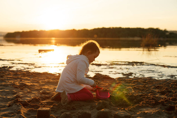 a girl plays with sand on a sandy beach on the river Bank during sunset - Fotoğraf, Görsel