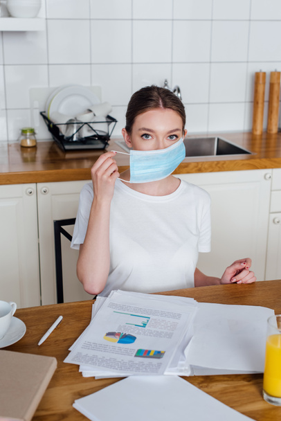 young woman wearing medical mask near charts and graphs on table - Photo, Image
