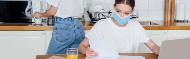 panoramic concept of woman in medical mask looking at blank paper near sister  - Foto, Imagen
