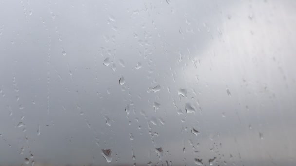 Zbliżenie filmiku z kroplami deszczu kapiącymi na szybę okienną. Ciemne zachmurzone niebo - Materiał filmowy, wideo
