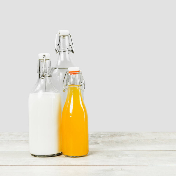 Drei Glasflaschen mit Milchwasser und Orangensaft auf grauer Holzoberfläche. Umweltfreundlicher Lebensstil und Einkaufen. Gesunde Ernährung verantwortungsvoll, Null-Abfall-Konzept. Kopierraum. Minimal. - Foto, Bild