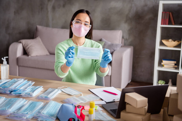 Photo of asian business lady blogger organize orders facial flu masks showing ready product web camera process preparing packs delivery package safety home office quarantine indoors - Valokuva, kuva