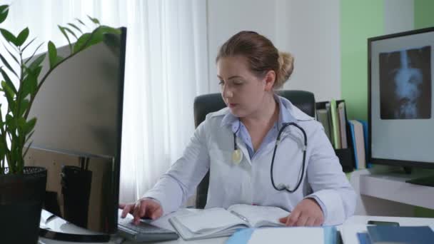 nő orvos beszél a beteggel keresztül video chat és a betegség tüneteinek rögzítése orvosi könyvben, modern orvostudomány - Felvétel, videó