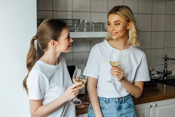 Smiling sisters holding glasses of wine in kitchen  - Foto, imagen
